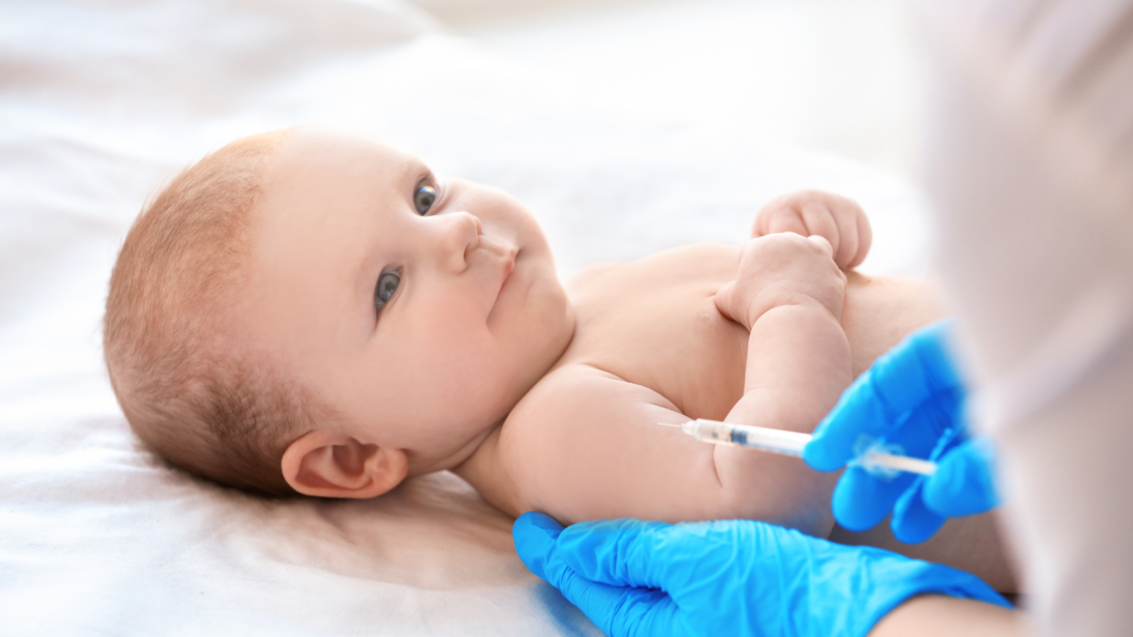baby lying down whilst having a vaccination by a doctor wearing blue medical gloves