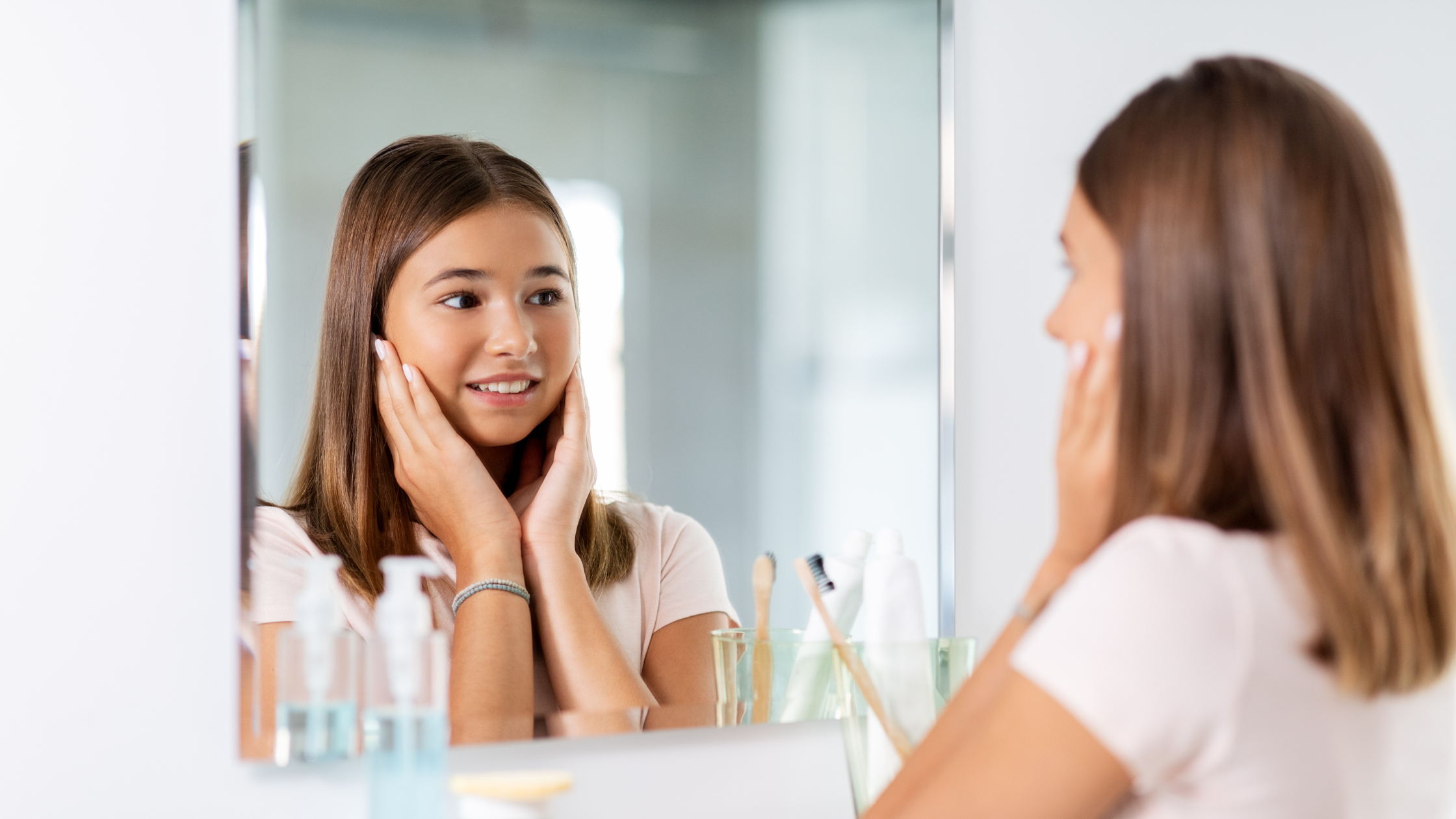 a young girl looking at herself in the mirror, studying her face and smiling