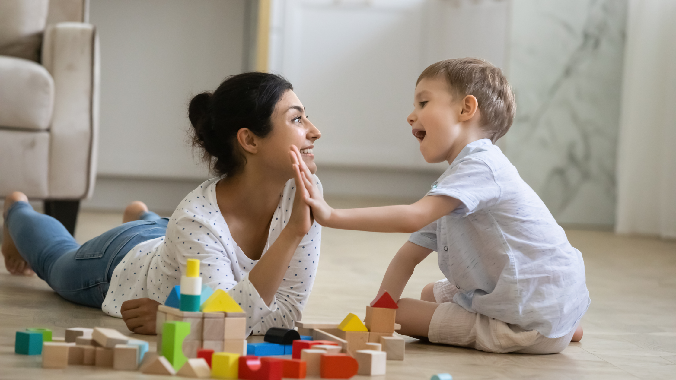A mum lying on the floor playing with her young son and giving him a high five to praise him