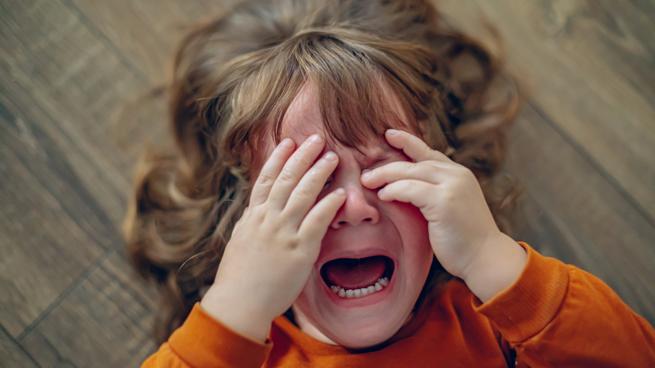a little girl lying on the floor with her hands over her face crying and having a tantrum