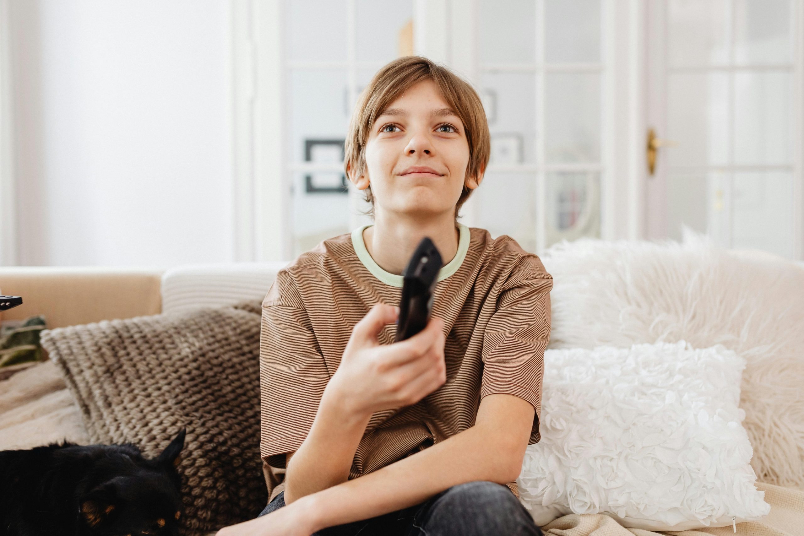 young boy sat on the sofa with the TV remote in his hand
