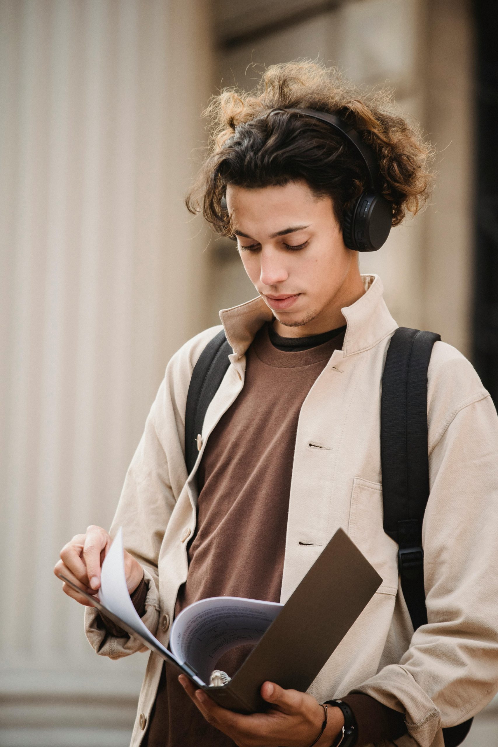 teenager with headphones and a backpack looking at his book