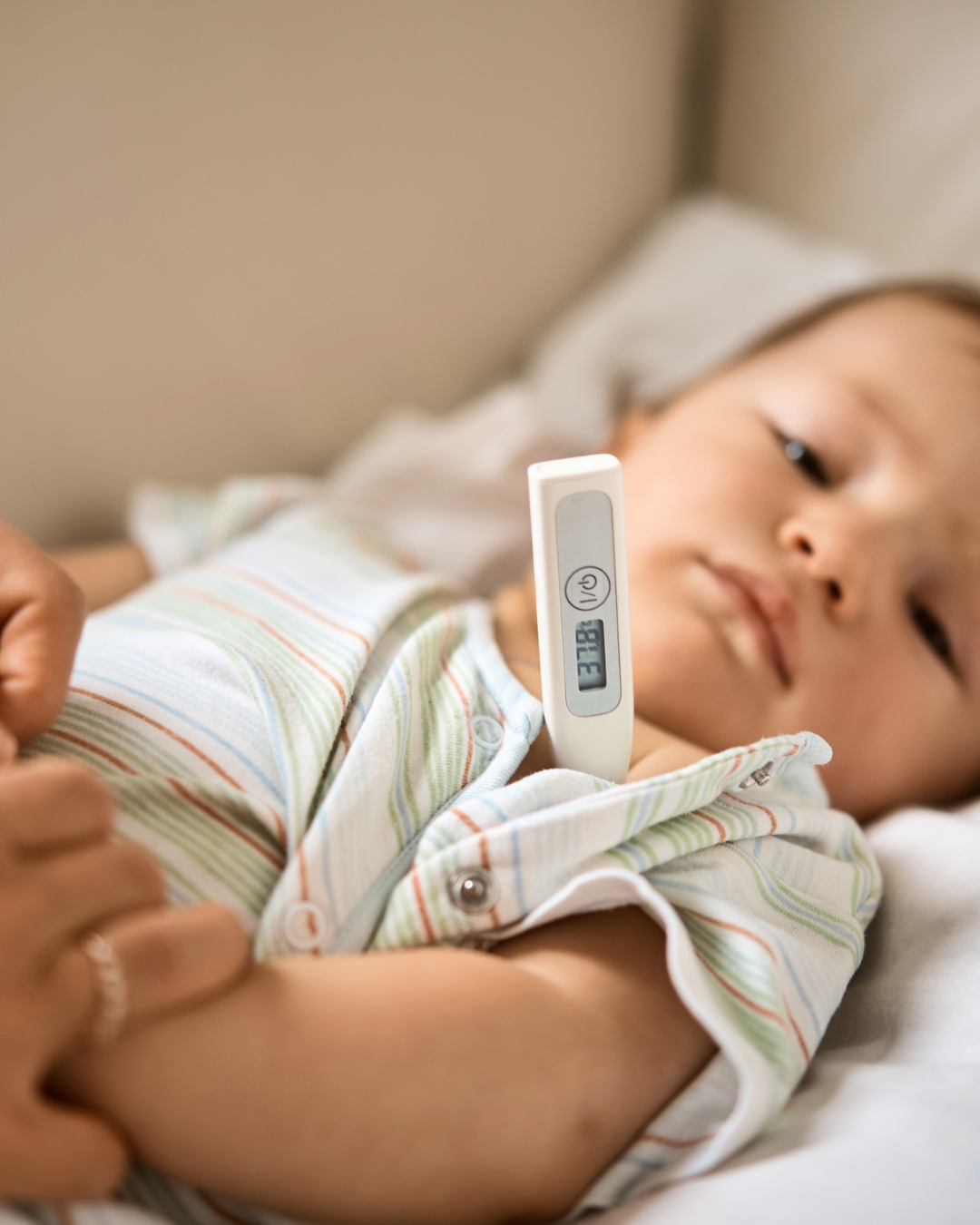 baby in bed with parent measuring their temperature